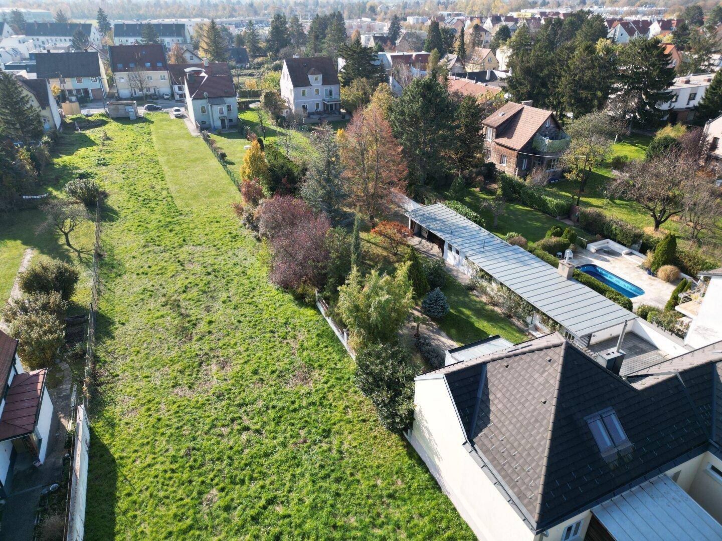 Luftaufnahme einer Wohnsiedlung mit Einfamilienhäusern und ausgedehnten Grünflächen unter blauem Himmel.