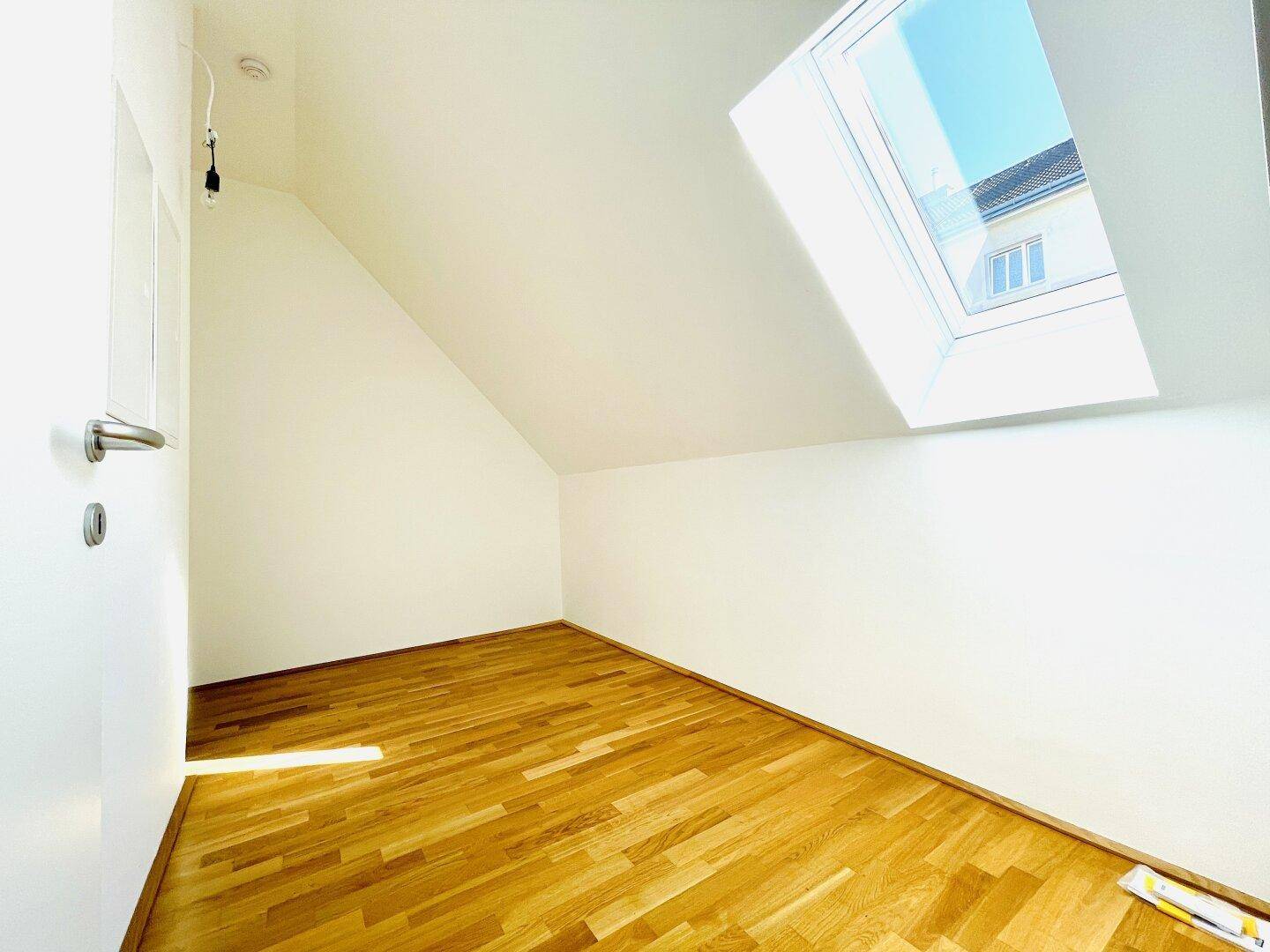 Helles Dachzimmer mit schräger Decke, Parkettboden und großem Dachfenster für viel Licht.