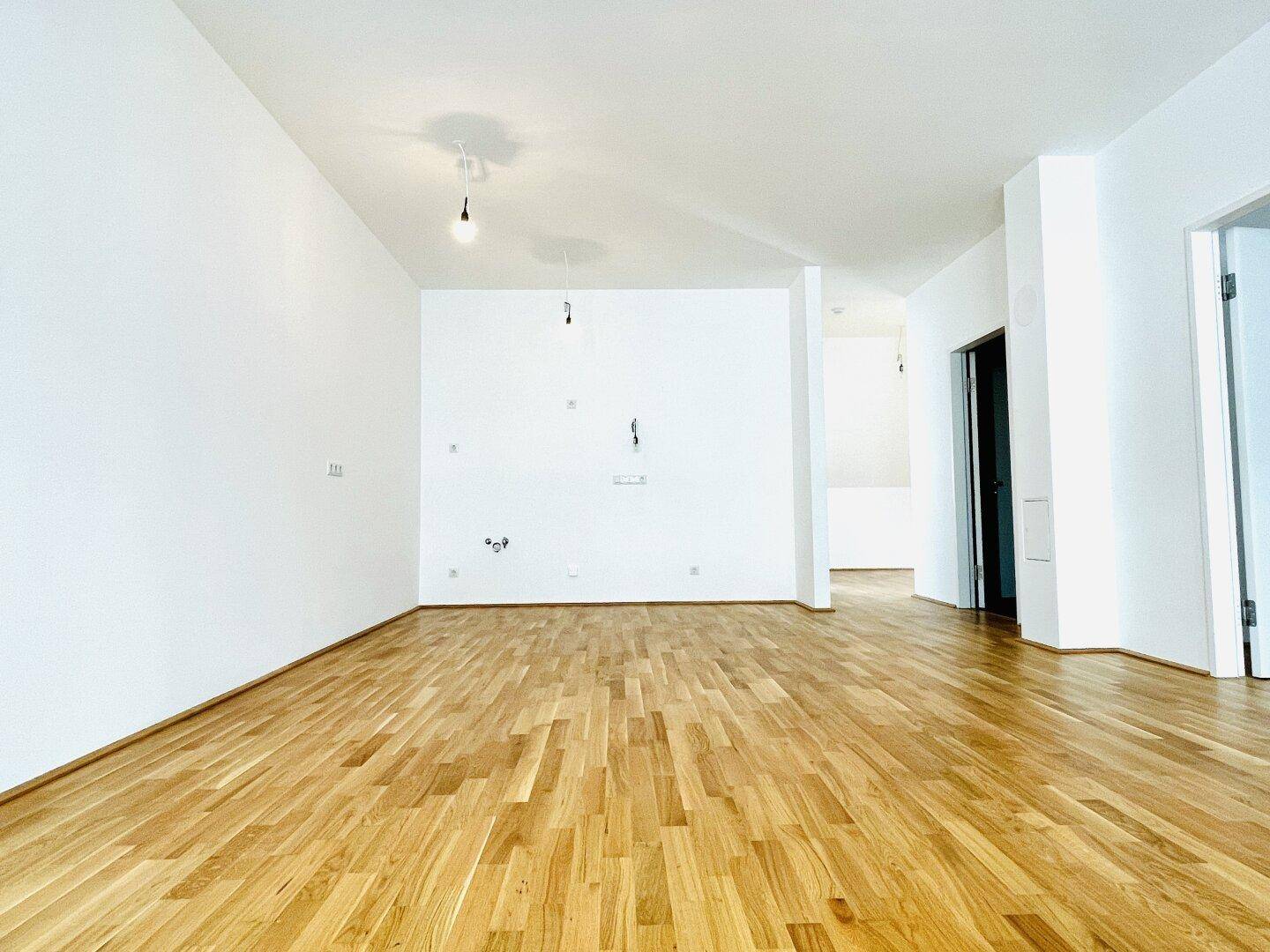 Geräumiges, leeres Zimmer mit hellem Parkettboden und weißen Wänden, ideal für Wohnbereich.