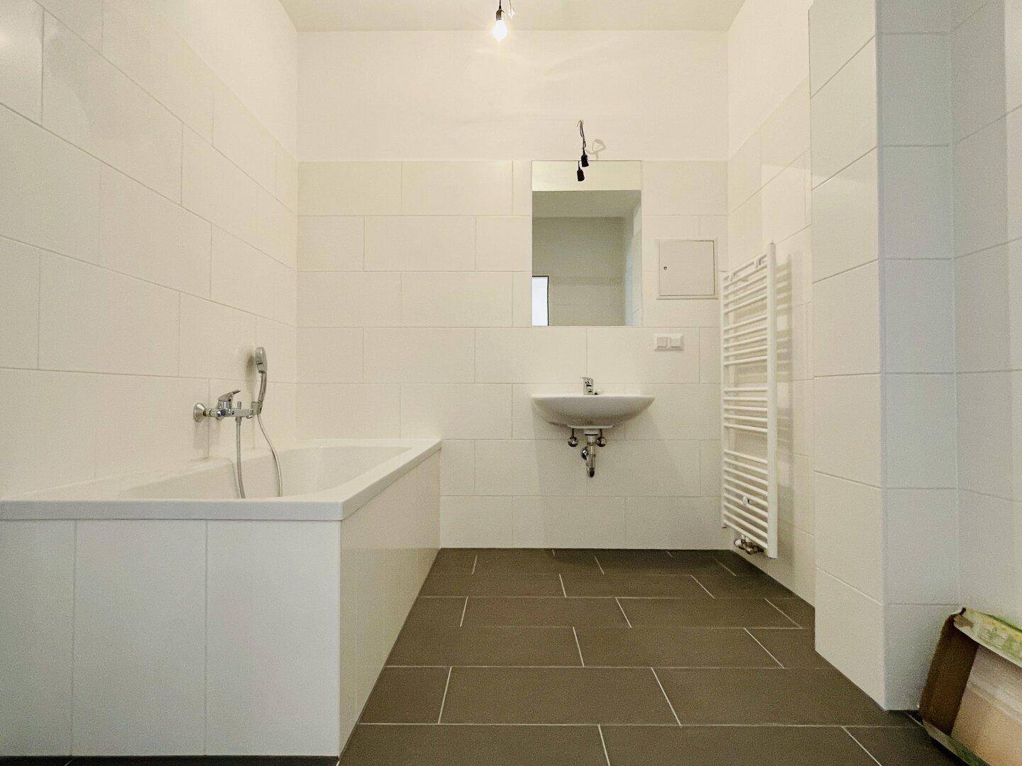 Modernes Badezimmer mit Badewanne, Waschbecken und weißen Wandfliesen sowie dunklem Boden.