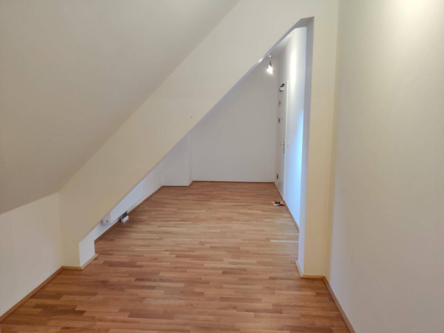 Leerer Raum im Dachgeschoss mit schräger Decke und hellem Parkettboden, vielseitig nutzbar.