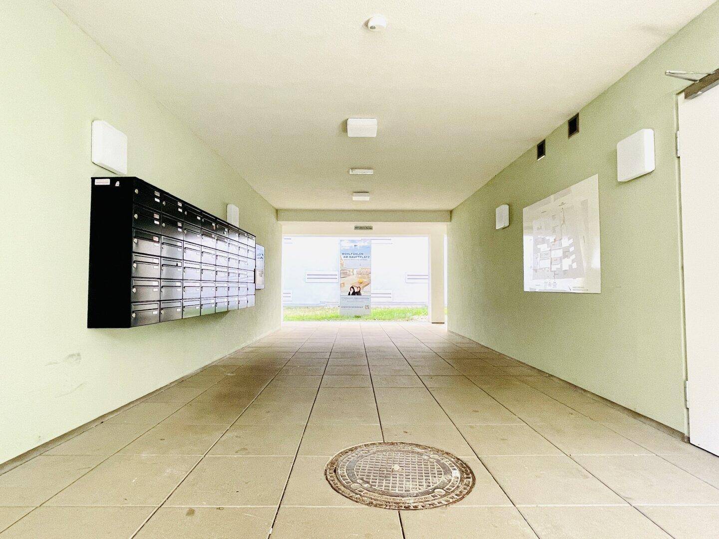 Heller Eingangsbereich mit Briefkästen an der Wand und Fliesenboden, führt ins Freie.