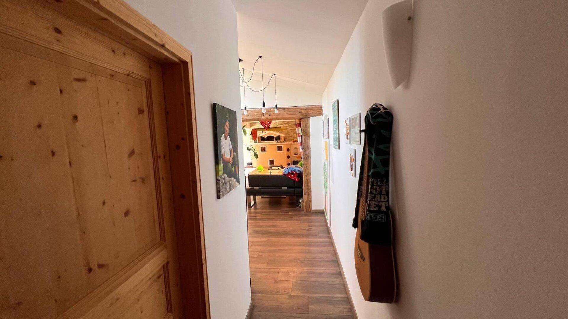 Langer Flur mit Holzboden, weißen Wänden und Bildern, der zu weiteren Räumen führt.
