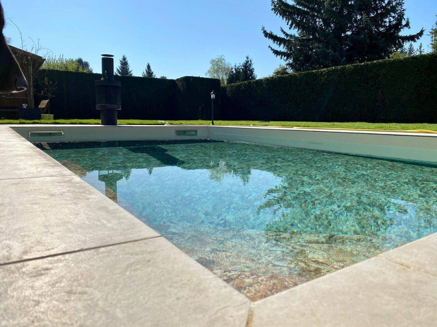 Nahaufnahme des Pools mit klarem Wasser und hellen Steinumrandungen unter blauem Himmel.