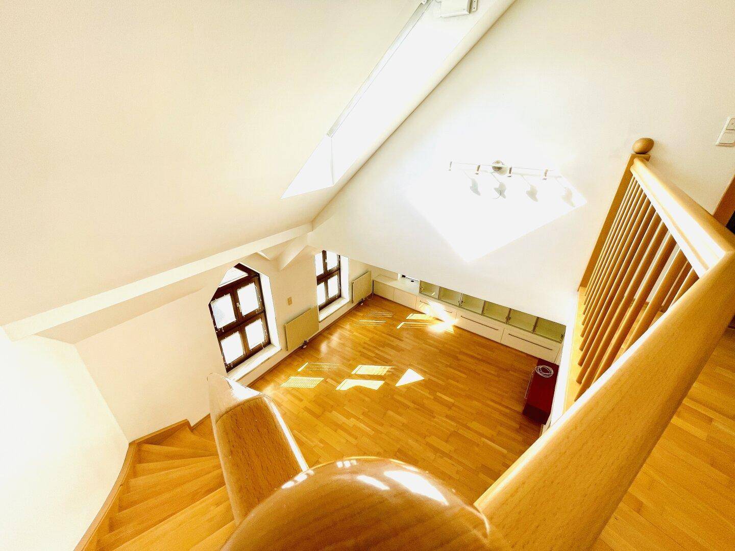Heller Wohnbereich im Dachgeschoss mit Holztreppe, Parkettboden und schrägen Decken.
