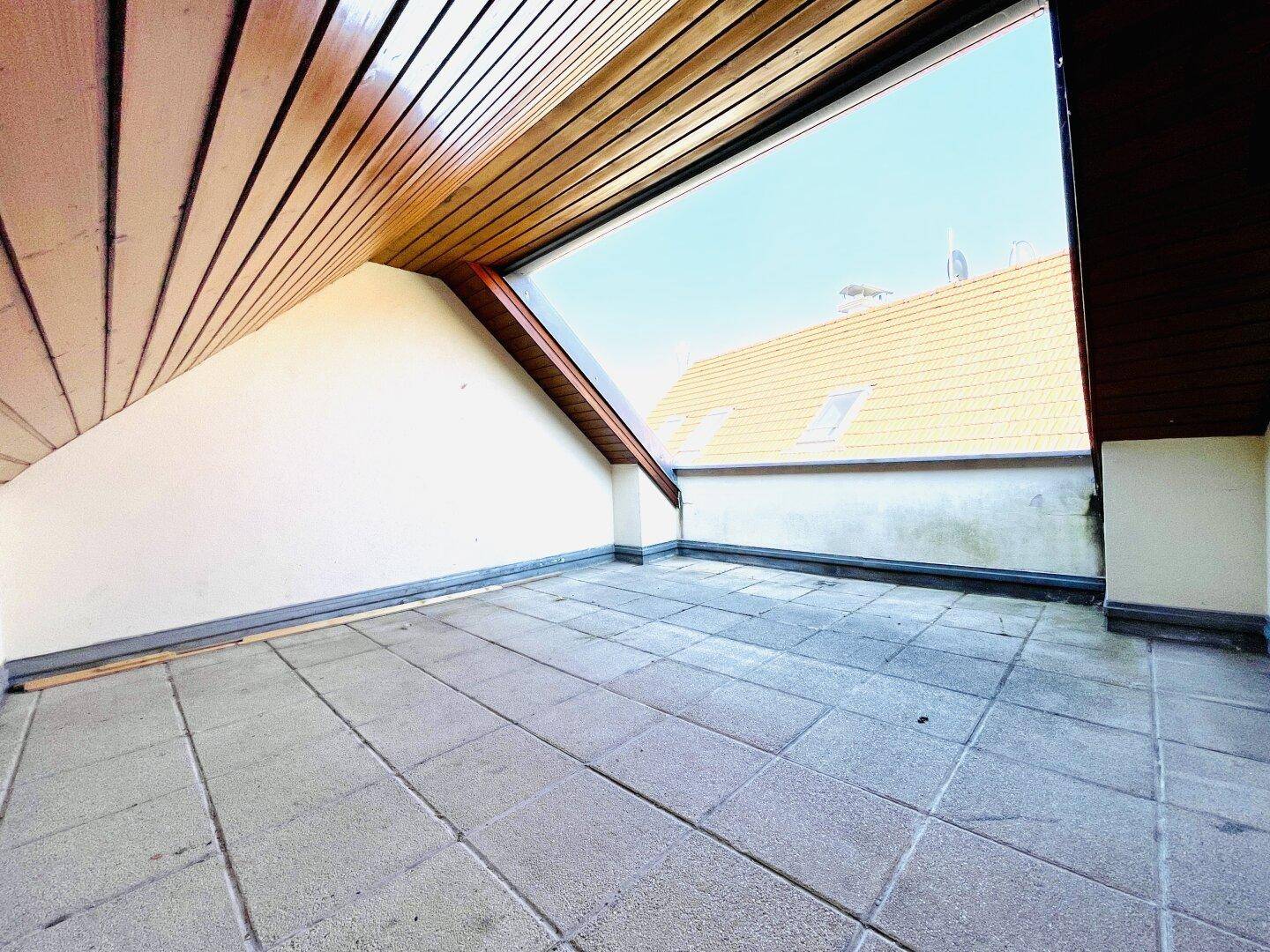 Geräumige Dachterrasse mit Fliesenboden, Holzverkleidung und Blick auf umliegende Dächer.
