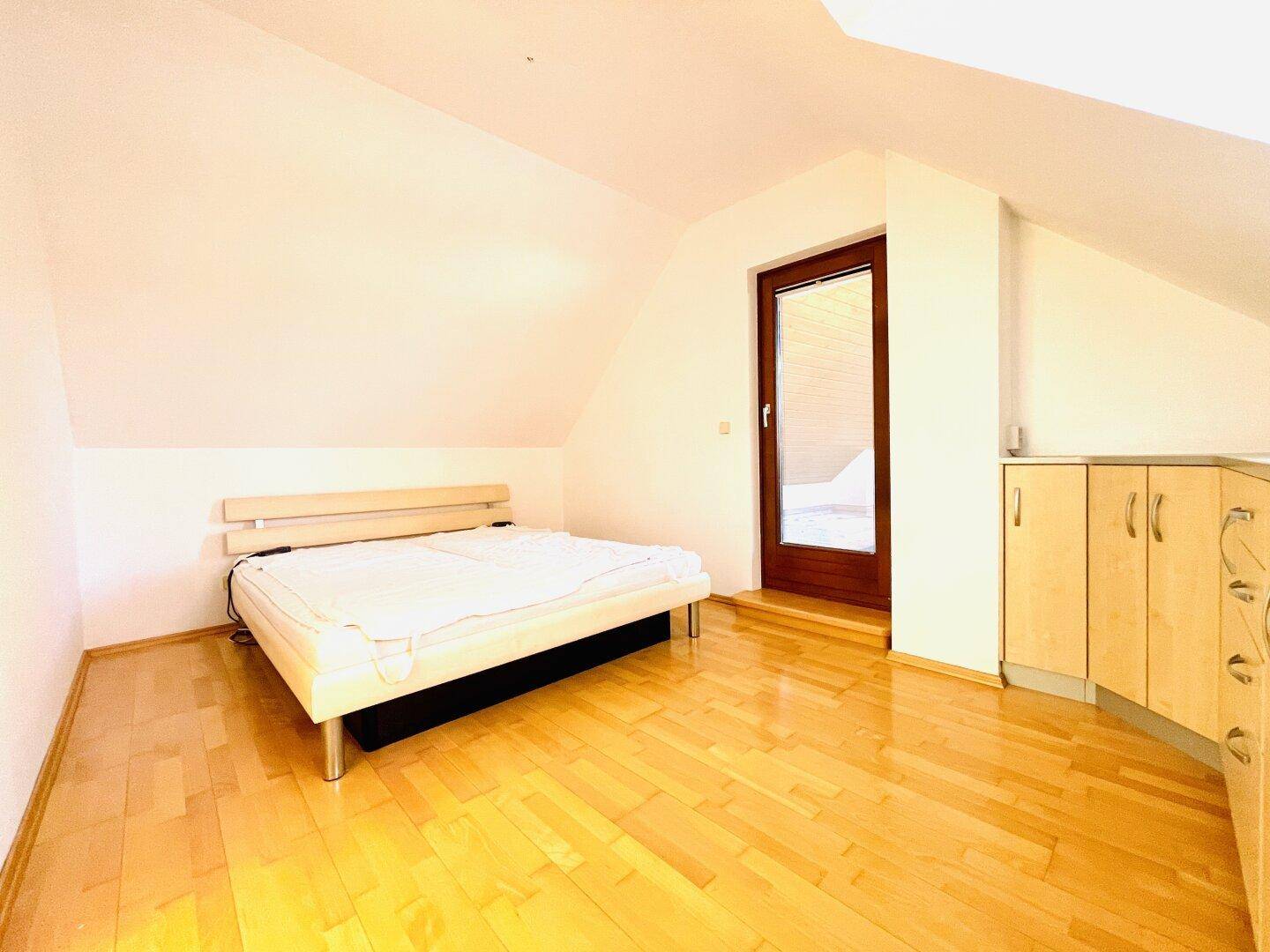 Schlafzimmer im Dachgeschoss mit Holzboden, schräger Decke und Zugang zu einem Außenbereich.