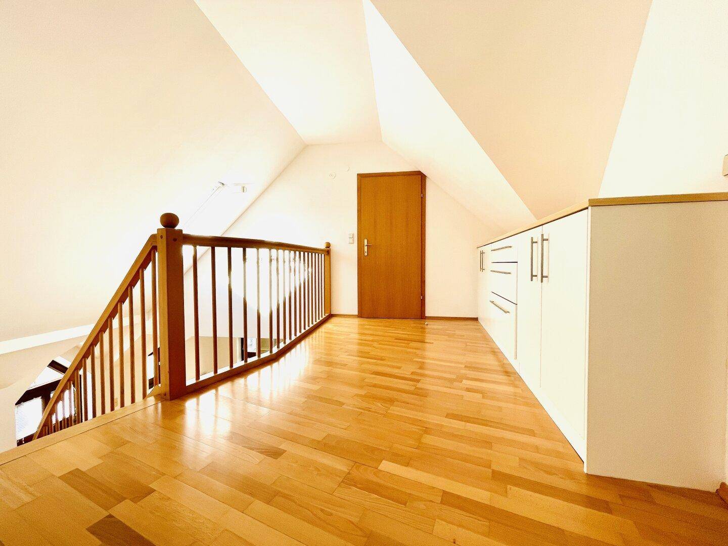 Heller Flur im Dachgeschoss mit Parkettboden, Einbauschränken und Holzgeländer.