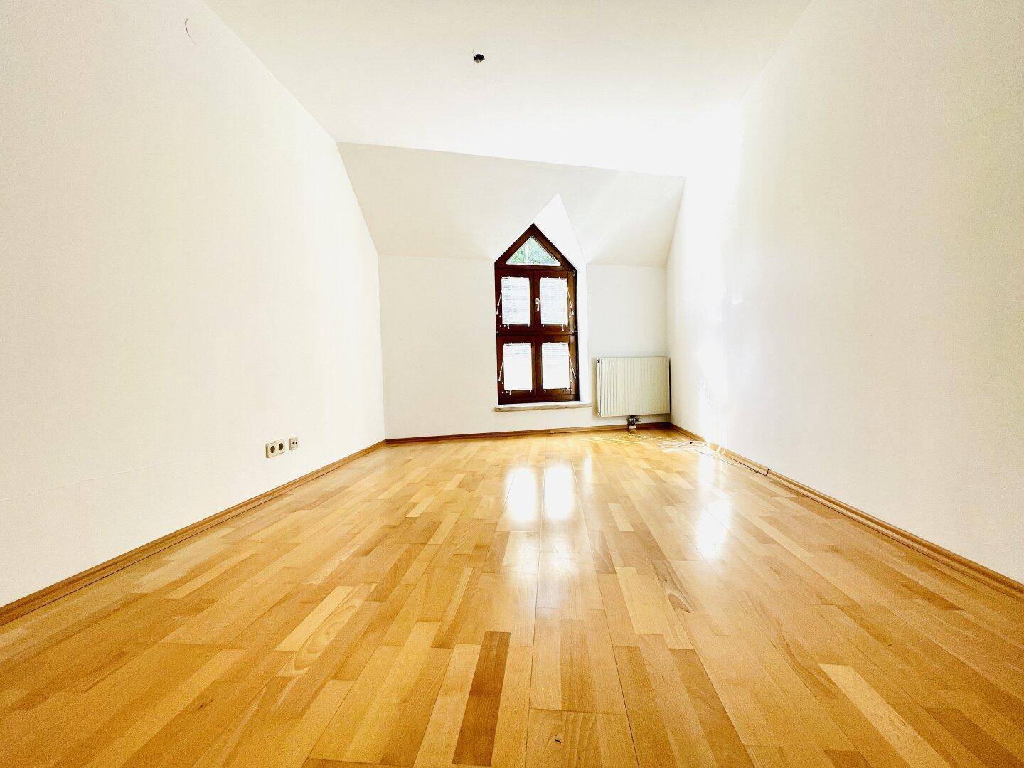 Helles Zimmer mit Parkettboden, schräger Decke und charakteristischem Bogenfenster.