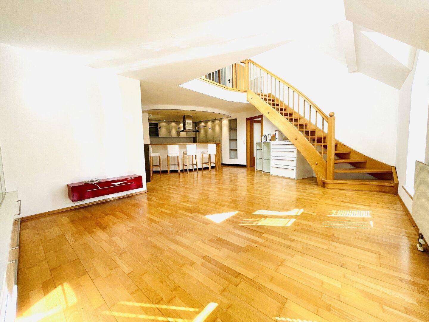 Großzügiger offener Wohnbereich mit Holzboden, Treppe und Blick auf die Küche.