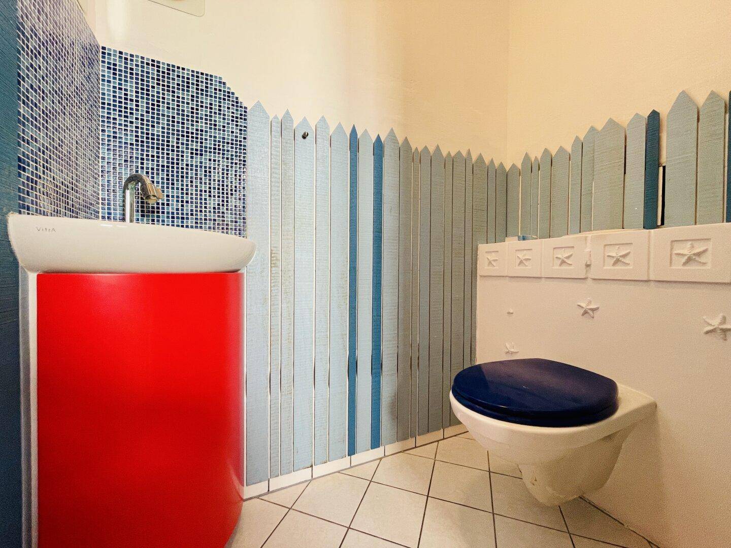 Originelles Gäste-WC mit rotem Waschtisch, blauen Mosaikfliesen und verspielter Wandgestaltung.