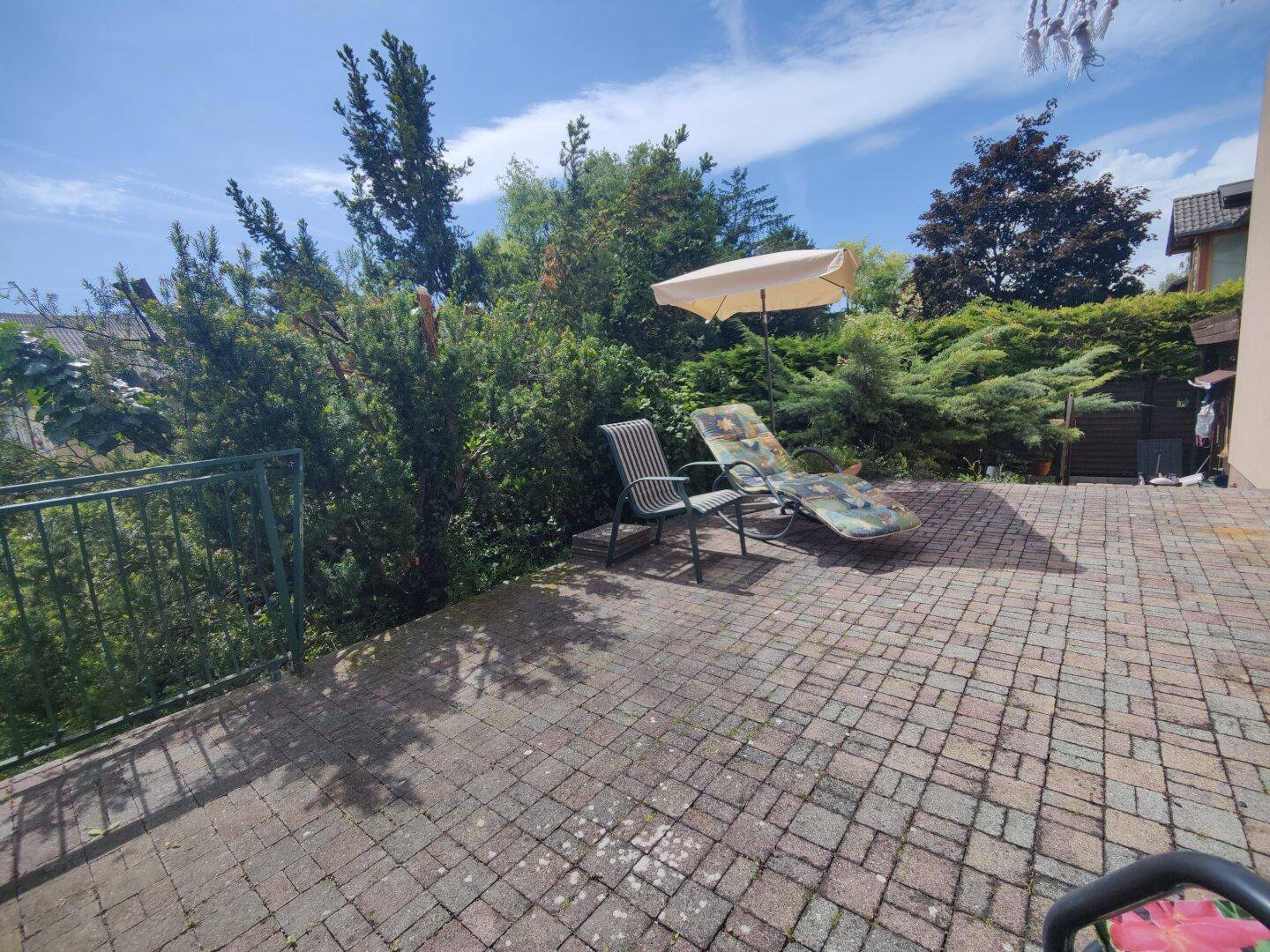 Geräumige gepflasterte Terrasse mit Liegestuhl und Sonnenschirm, ideal für sonnige Tage.