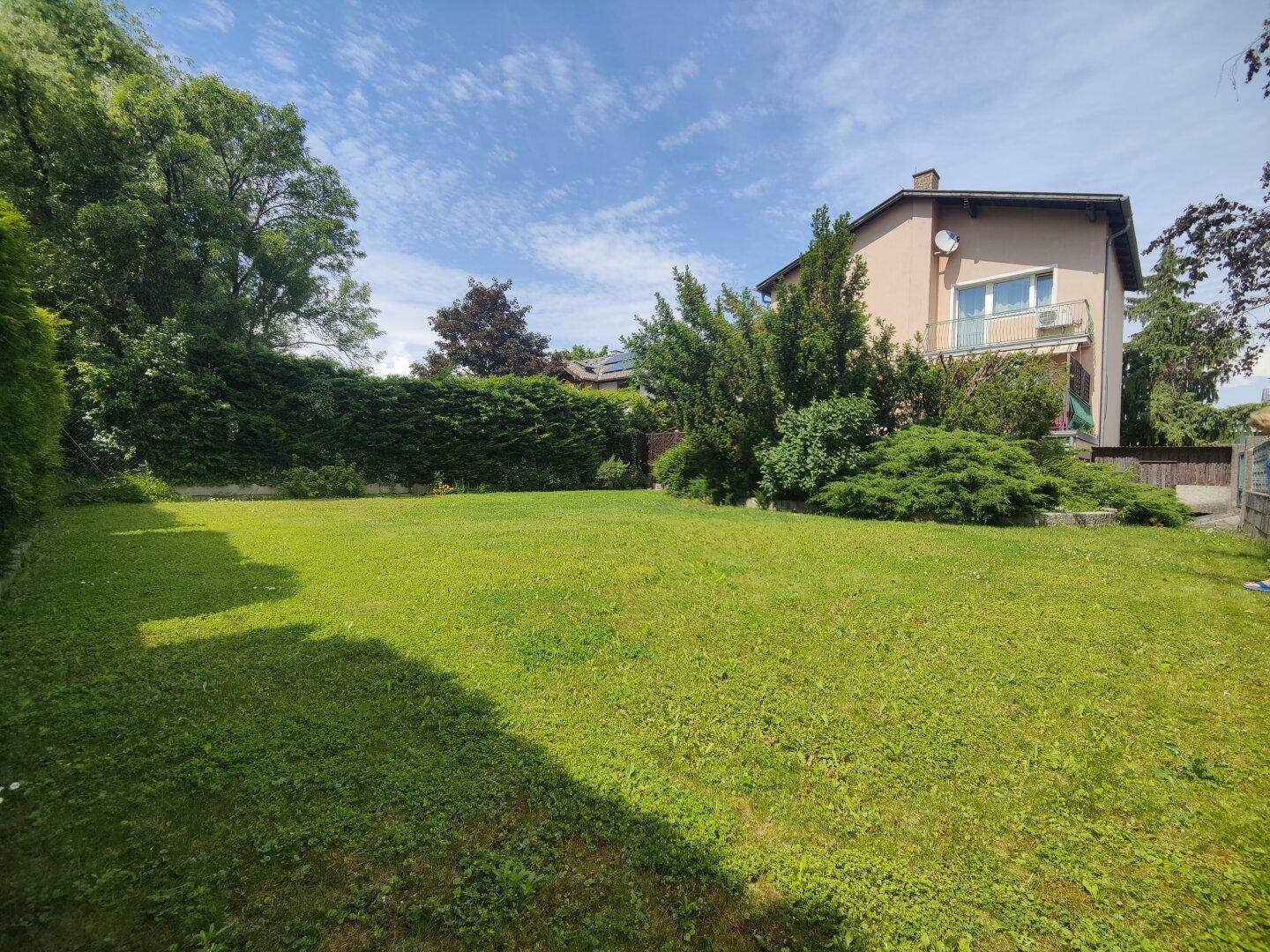 Großer, gepflegter Garten mit weitläufiger Rasenfläche und hoher Hecke, ideal zum Entspannen.