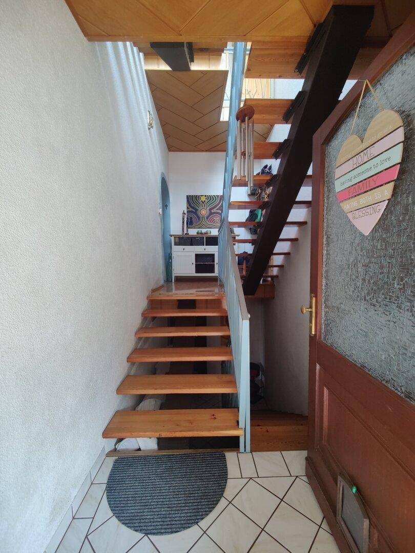 Heller Eingangsbereich mit Holztreppe, die in die oberen Stockwerke führt, und Fliesenboden.