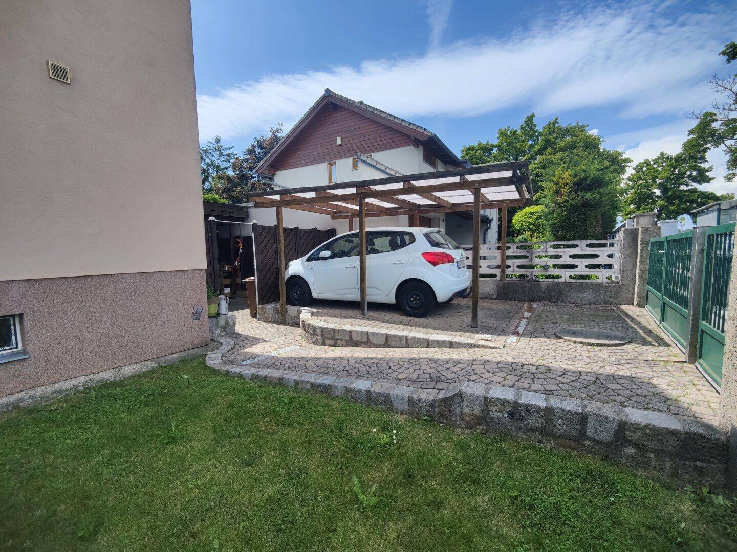 Überdachter Carport mit gepflasterter Einfahrt und zusätzlichem Stellplatz.