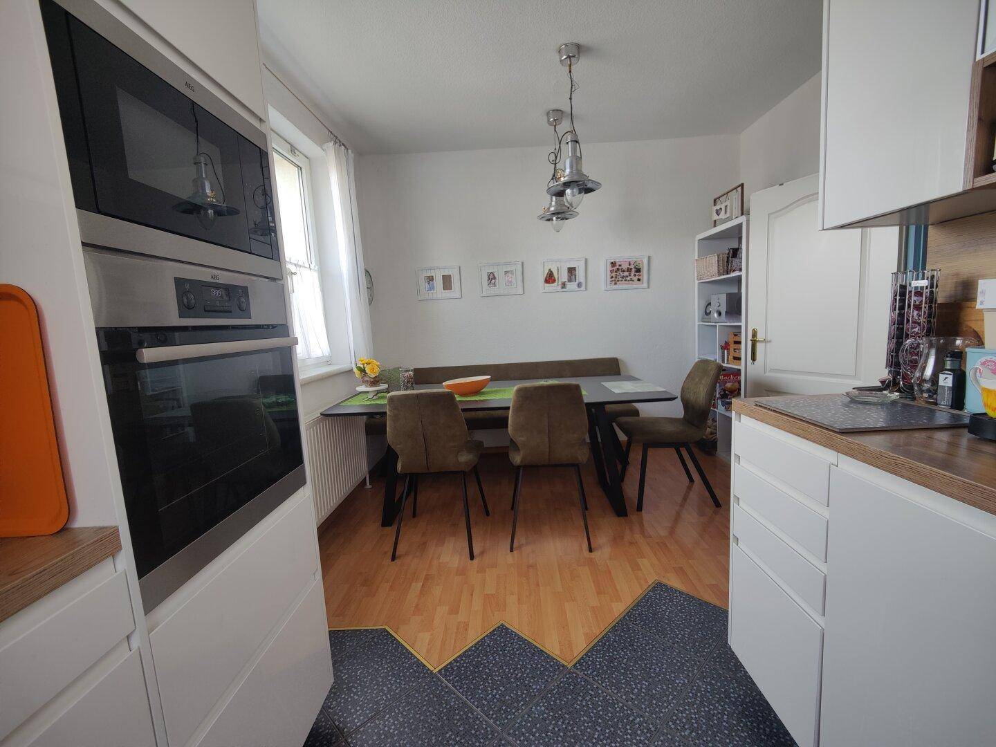 Moderne Wohnküche mit Esstisch, integrierten Geräten und hellem Fenster.
