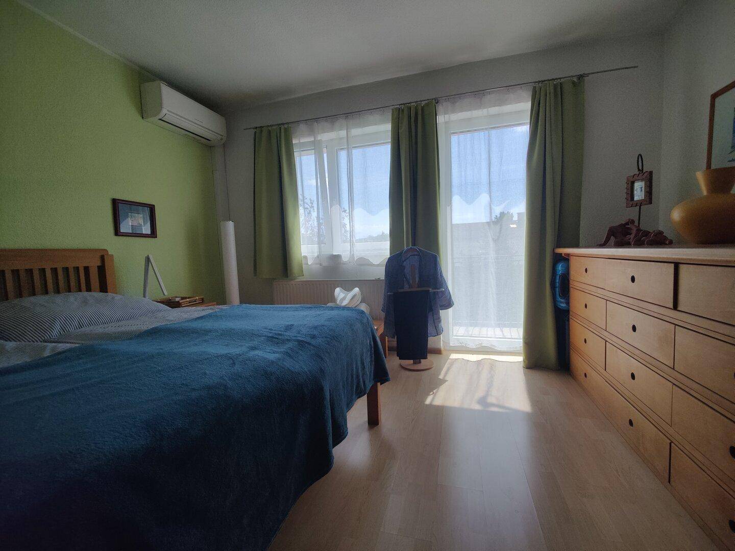 Helles Schlafzimmer mit Doppelbett, Holzkommode und Klimaanlage, mit Zugang zum Balkon.