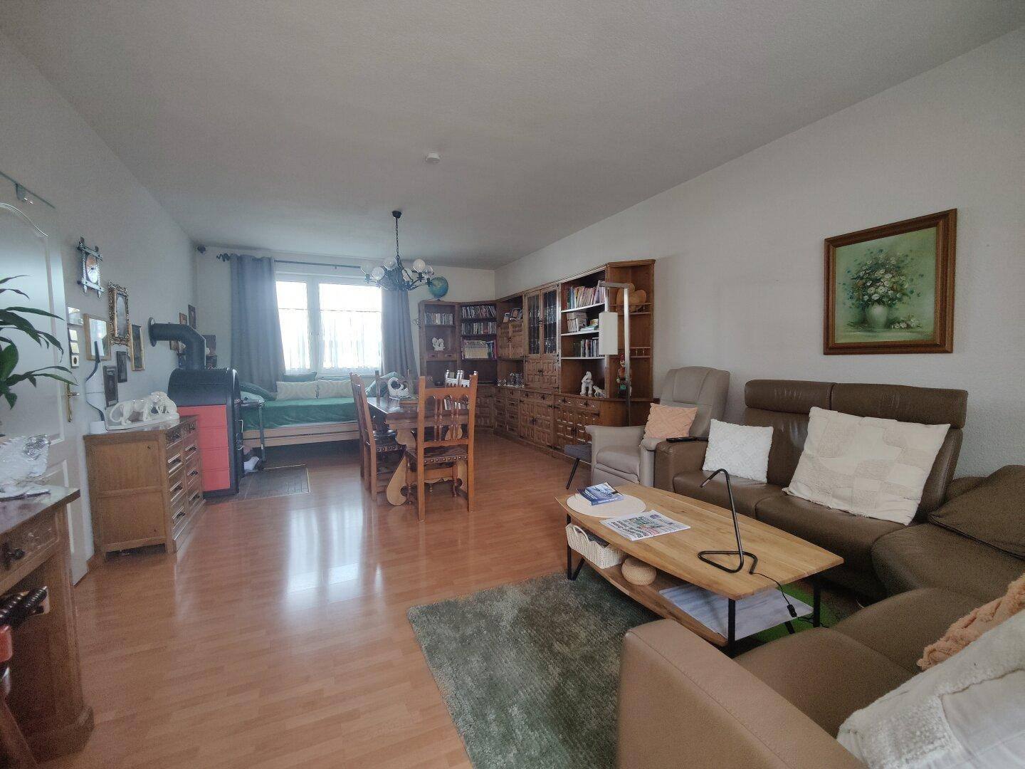Geräumiger Wohn-Essbereich mit Parkettboden, bequemen Sofas und einem Bücherregal.