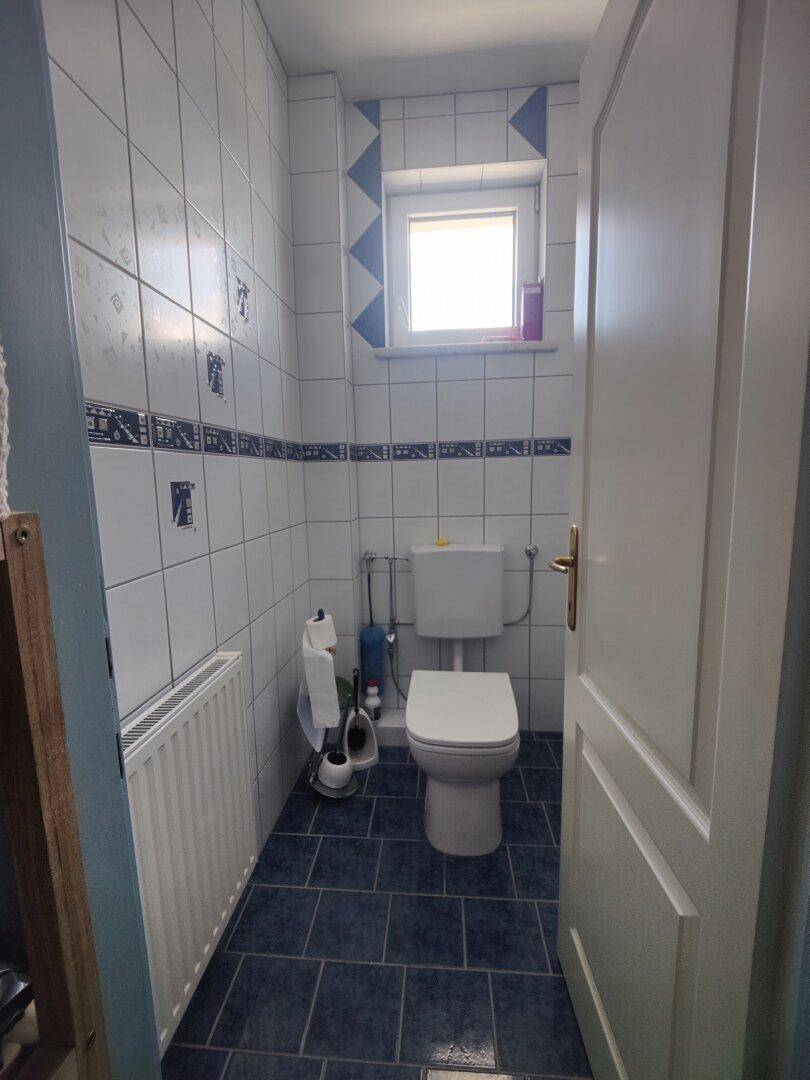 Kleines WC mit Fenster, blauen Fliesen und Heizkörper, funktional eingerichtet.