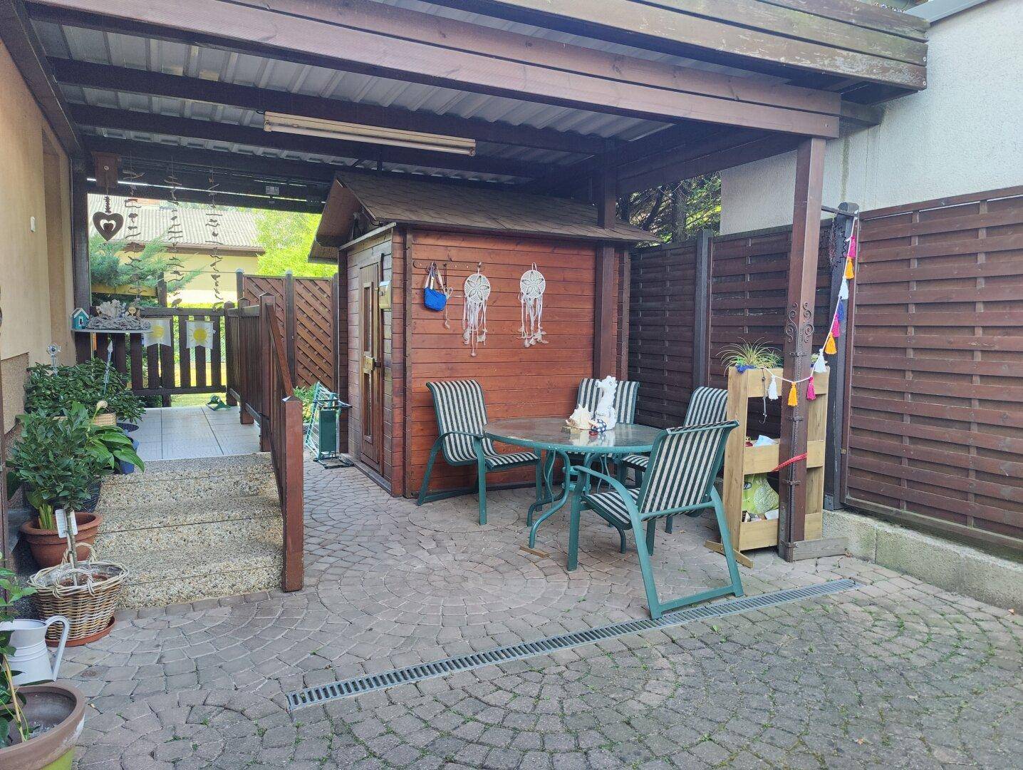 Überdachter Terrassenbereich mit Gartenmöbeln und einem Holzschuppen, perfekt für gesellige Stunden.