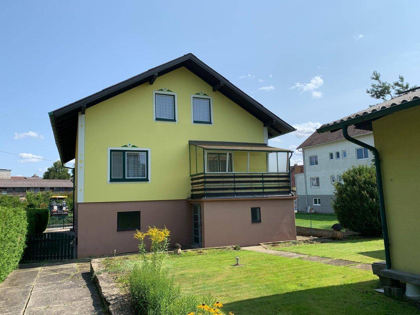 Rückansicht des gelben Hauses mit Balkon und gepflegtem Rasen im Gartenbereich.