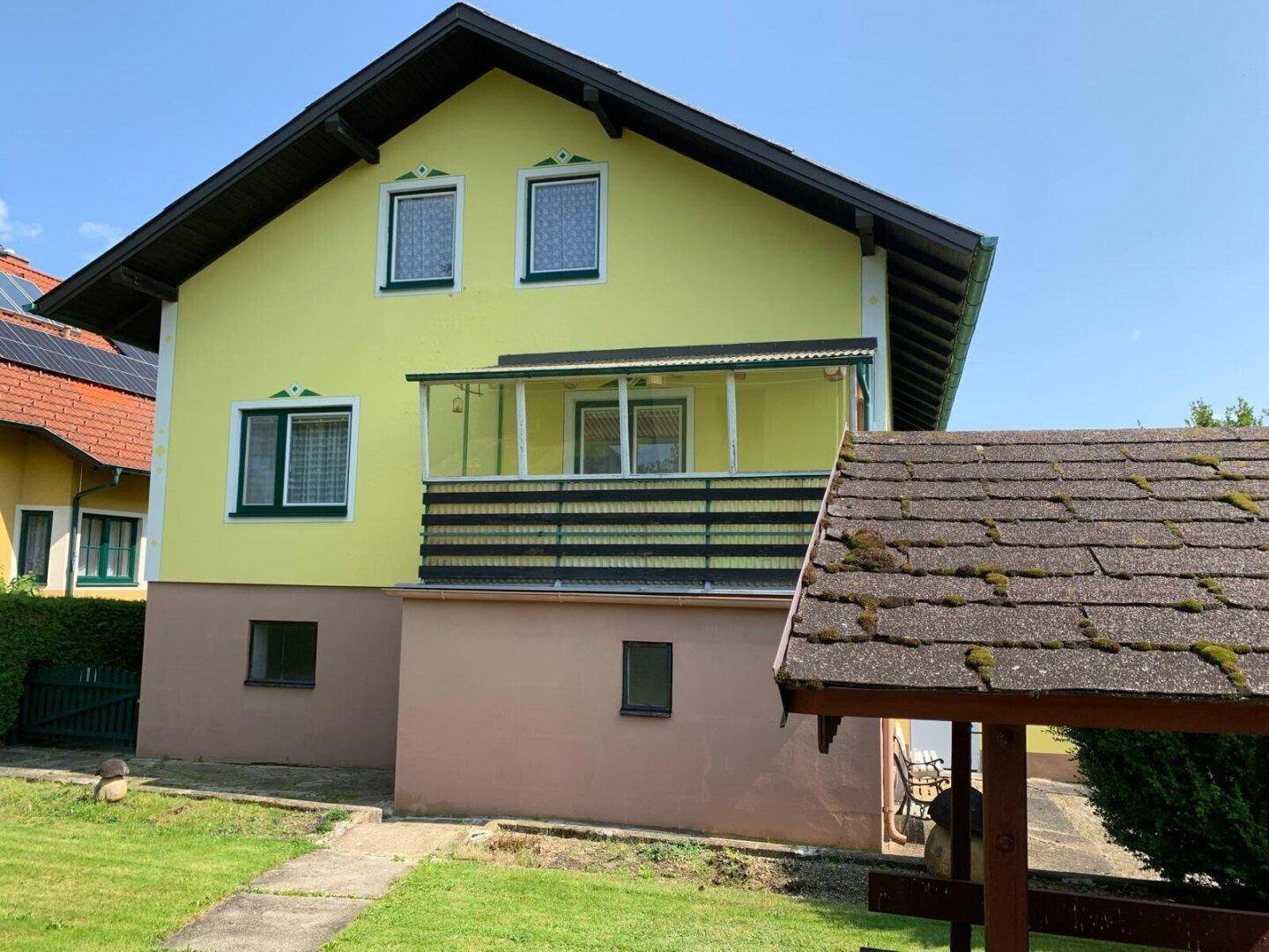 Rückseite des gelben Hauses mit Balkon und Blick auf den Garten mit Pavillon.