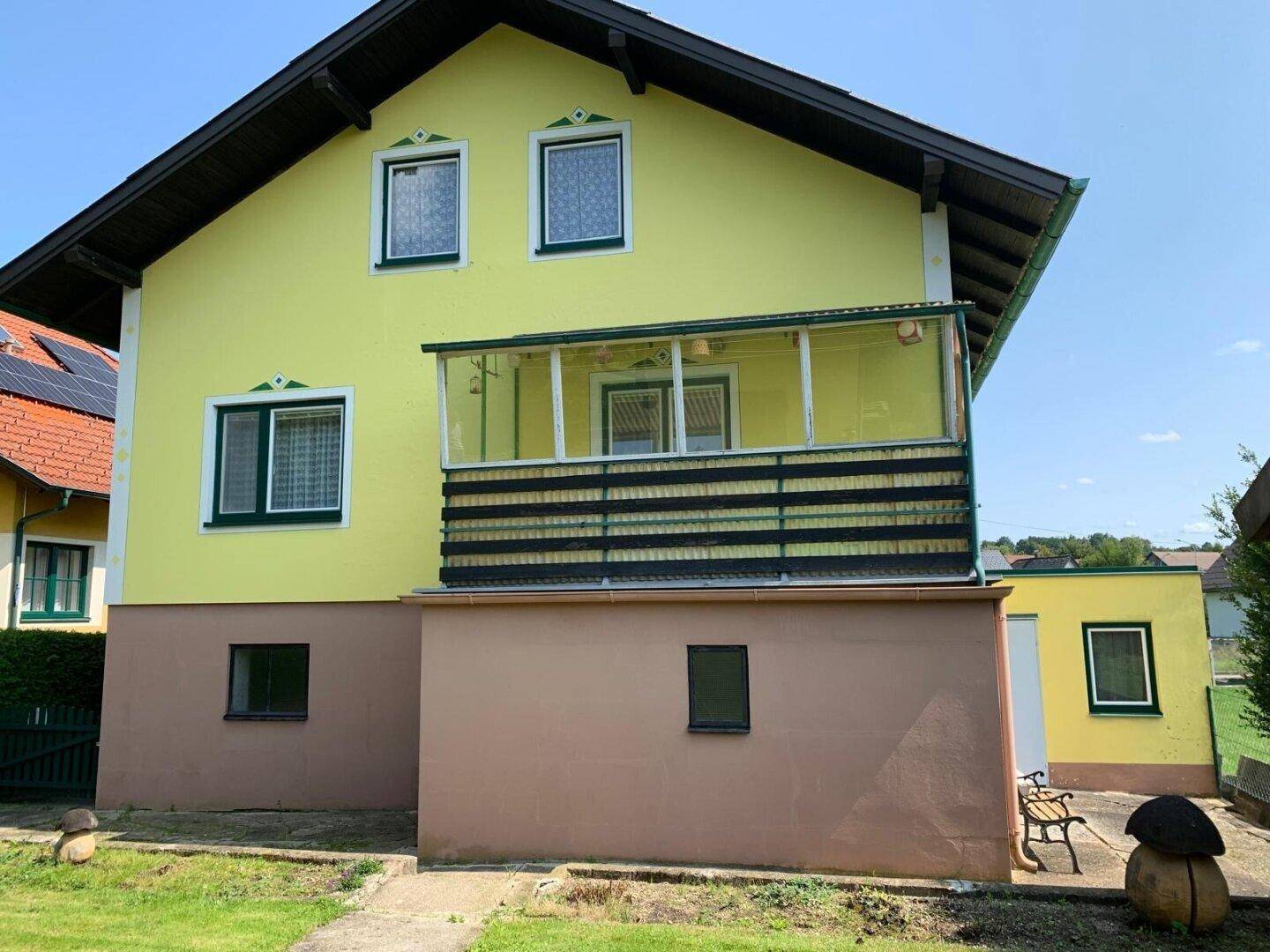 Gelbes Haus mit Balkon und Gartenbereich, inklusive einer kleinen Sitzbank im Freien.