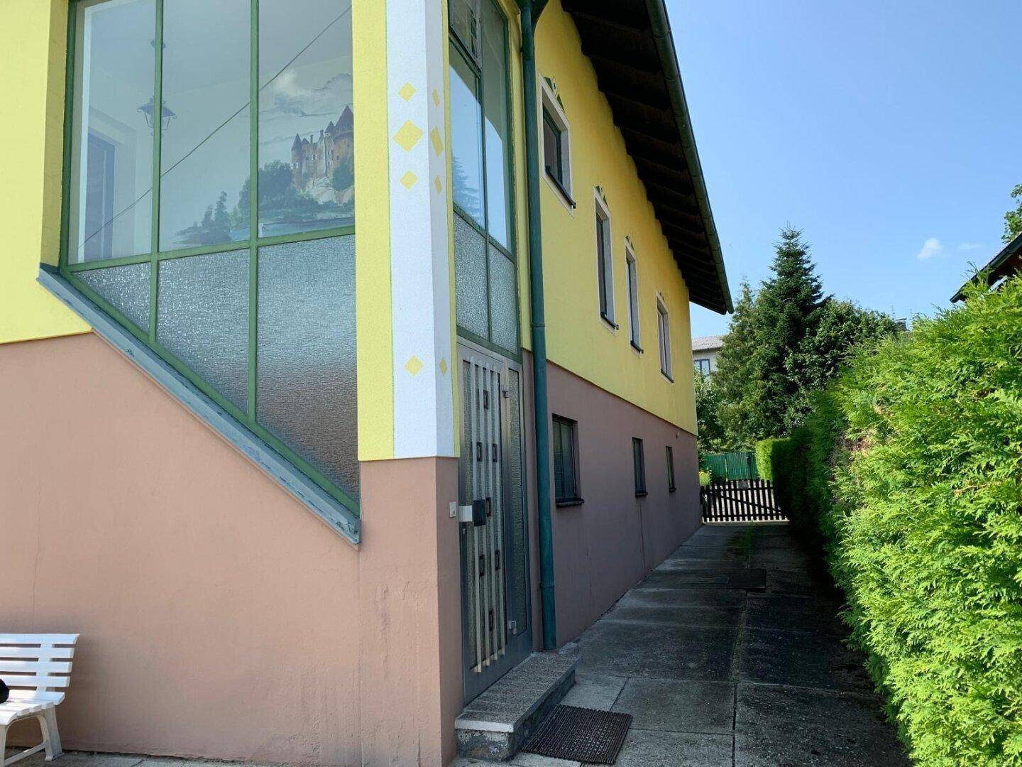 Seitenansicht des Hauses mit verglastem Anbau, Eingang und schmalem Zugangsweg.