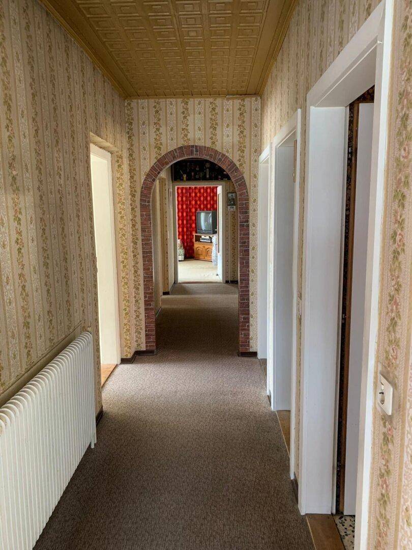 Langer Flur mit Teppichboden, gemusterter Tapete und Ziegelbogen.