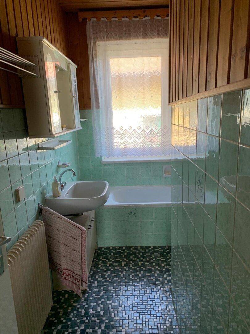 Badezimmer im 80er-Jahre-Stil mit grünen Fliesen, Badewanne und Holzverkleidung.