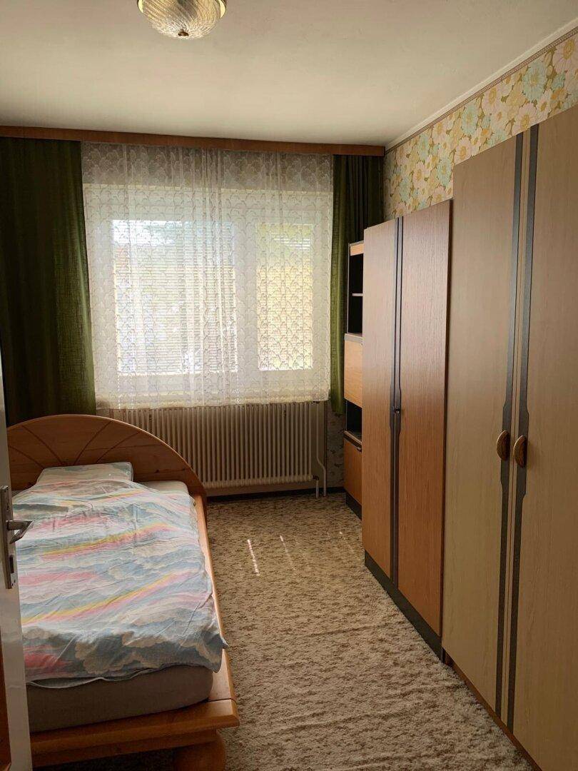 Schlafzimmer mit Einzelbett, Teppichboden und Holzschränken im klassischen Stil.