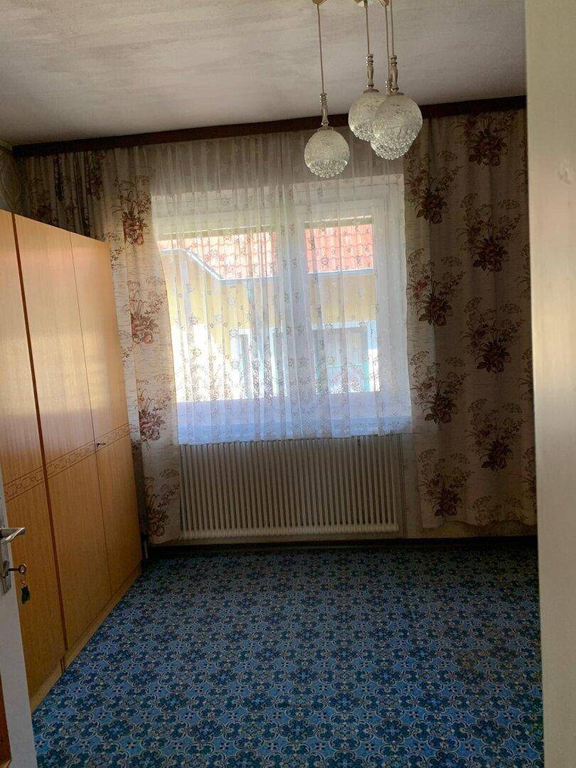 Schlafzimmer mit blau gemustertem Teppichboden und Holzschrank.