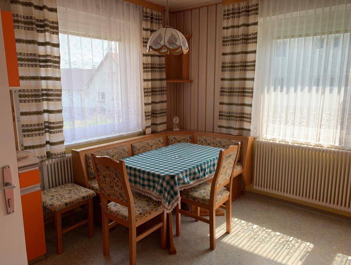 Gemütlicher Essbereich mit Eckbank, Holztisch und Fenstern mit Vorhängen.