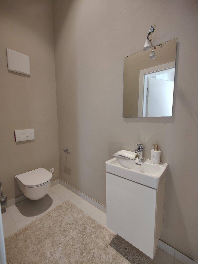 Modernes Gäste-WC mit wandhängender Toilette, Einzelwaschbecken und beigefarbenen Wänden.