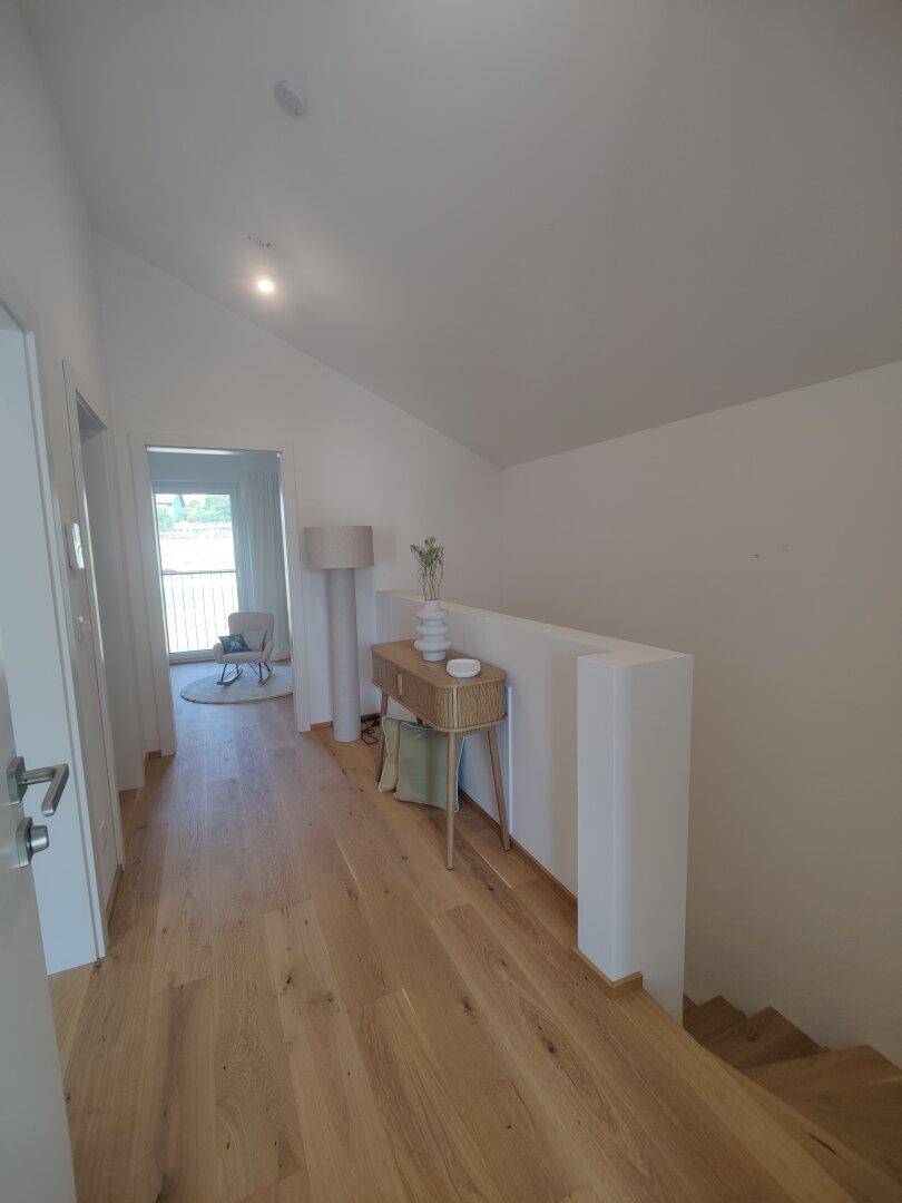 Heller Flur im Obergeschoss mit Dachschräge, Holzboden und Zugang zu weiteren Räumen.