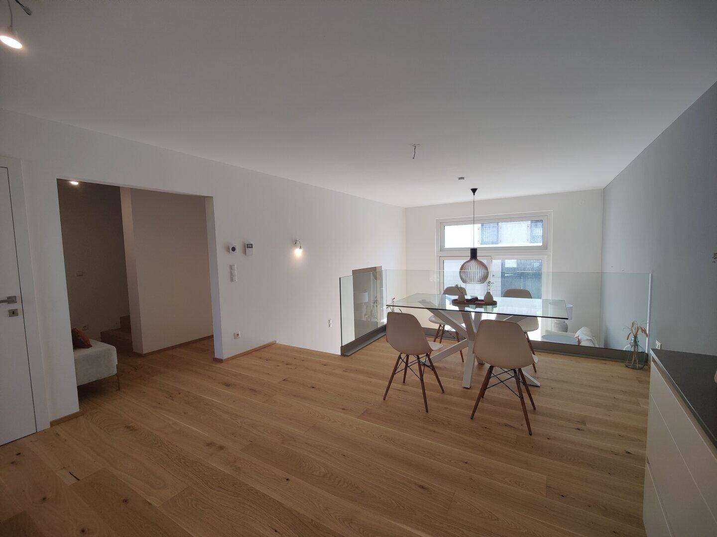 Moderner Essbereich mit Holzboden, Glastisch und Blick auf die Umgebung.