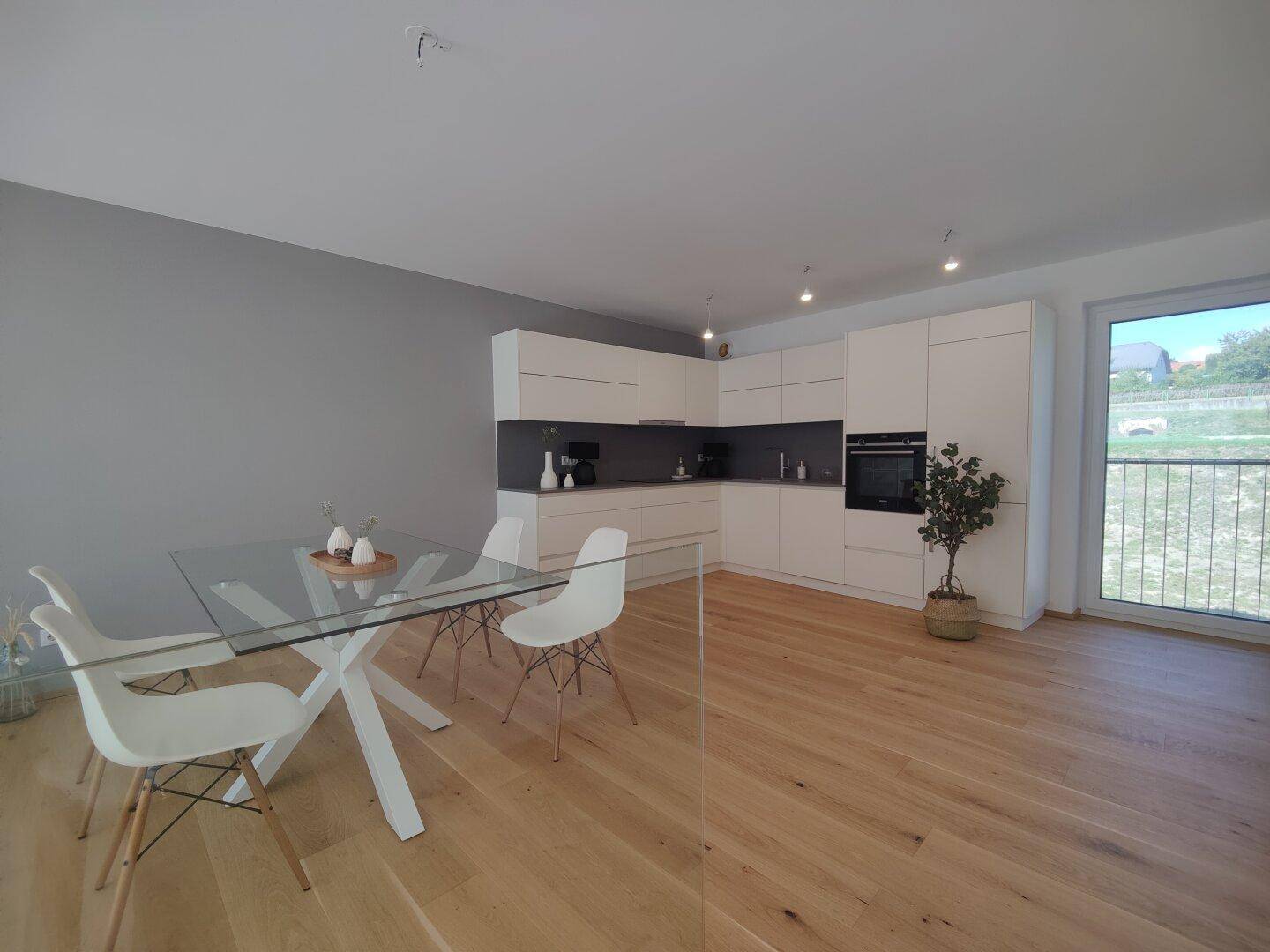 Moderne Einbauküche mit weißen Schränken, dunkler Arbeitsplatte und Essbereich.