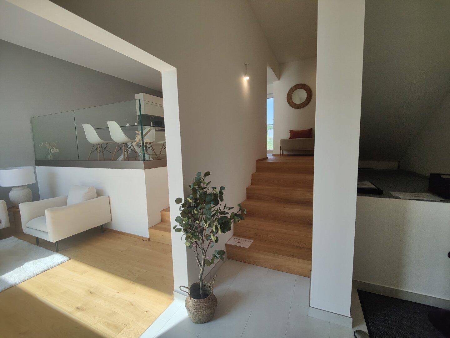 Heller Flur mit Holztreppe, Glasgeländer und Blick in den offenen Wohnbereich.
