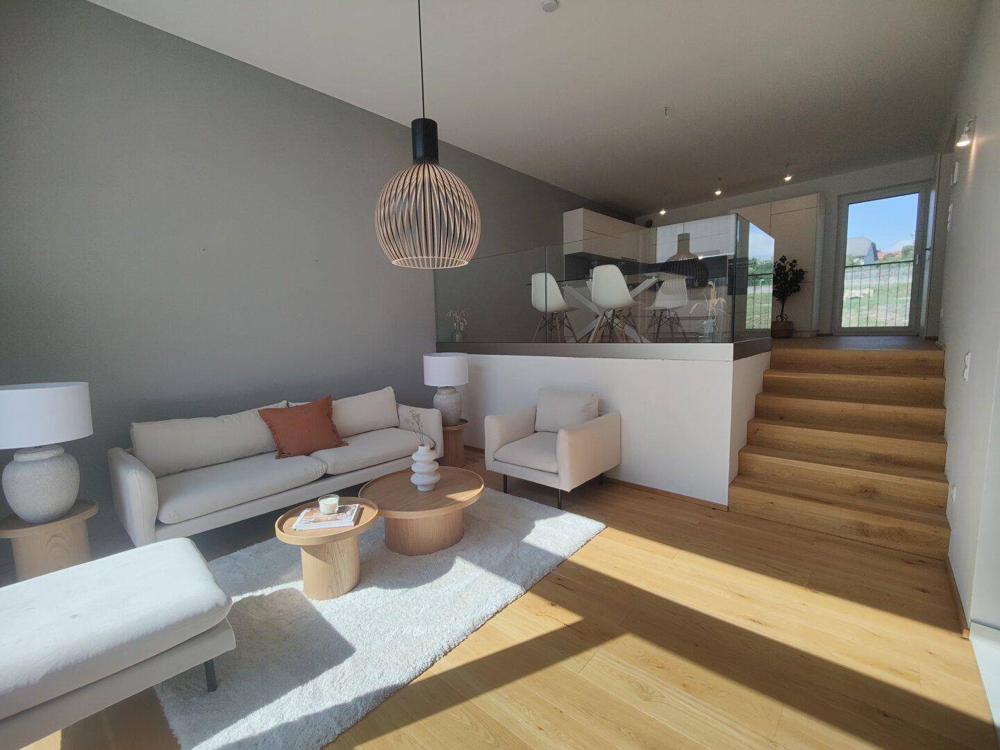 Gemütliches Wohnzimmer mit hellem Sofa, Holzboden und offener Verbindung zur Küche.