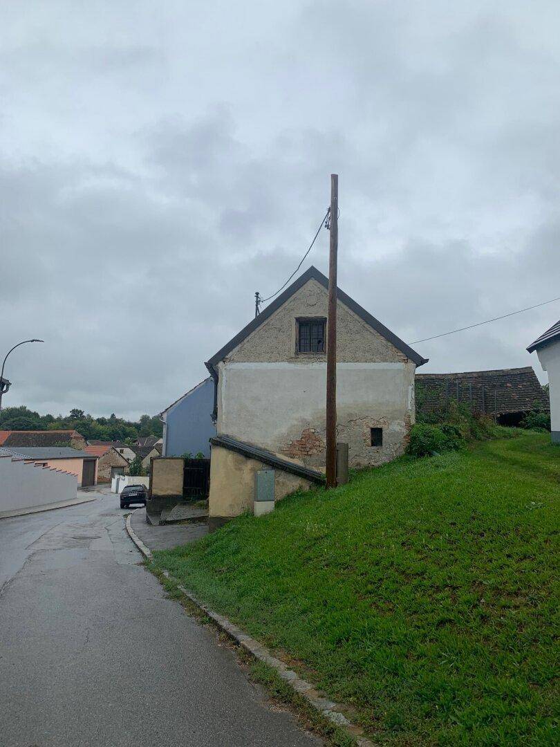 Seitenansicht eines älteren Hauses mit bröckelndem Putz und einem Fenster im Giebelbereich, an einer Straße.