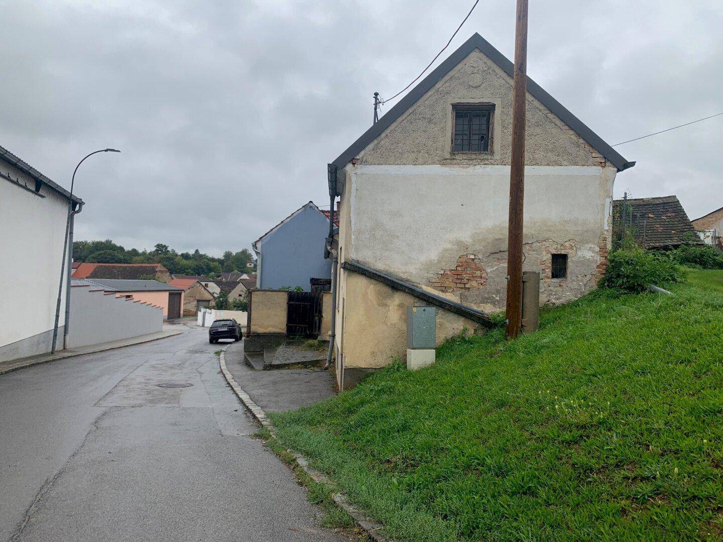 Rückansicht eines älteren Hauses mit bröckelndem Putz und einem Fenster im Giebelbereich, an einer Straße.