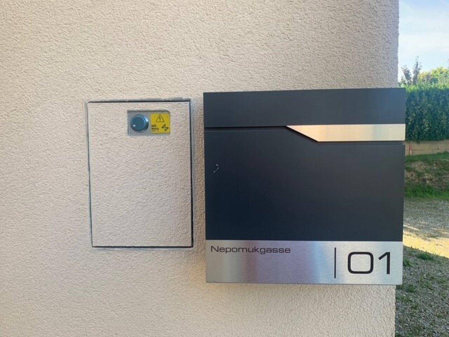 Moderne Hausnummer und Briefkasten an der Fassade eines Neubaus.