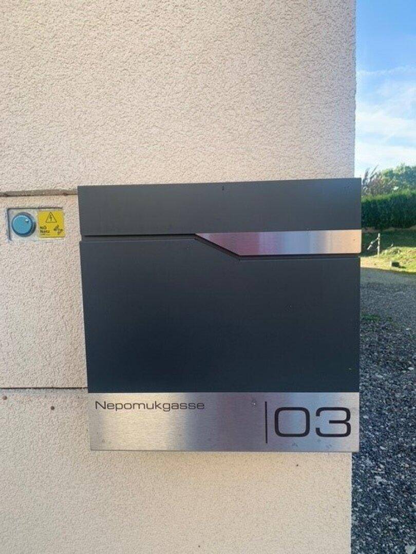 Moderner Briefkasten mit Hausnummer und Straßennamen an der Fassade.