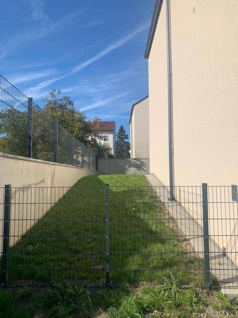 Seitenansicht eines Gebäudes mit einer begrünten Böschung und einem stabilen Zaun.