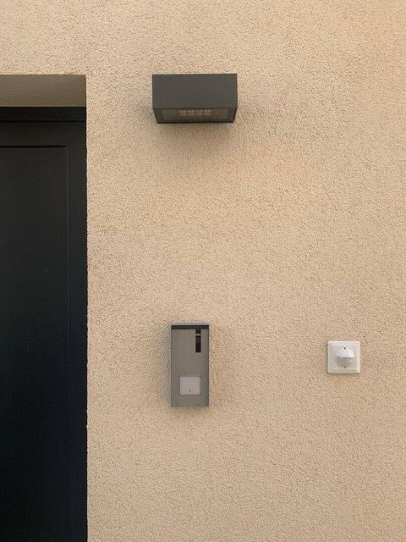 Außenwand mit moderner Beleuchtung, Briefkasten und Bewegungsmelder für Sicherheit.