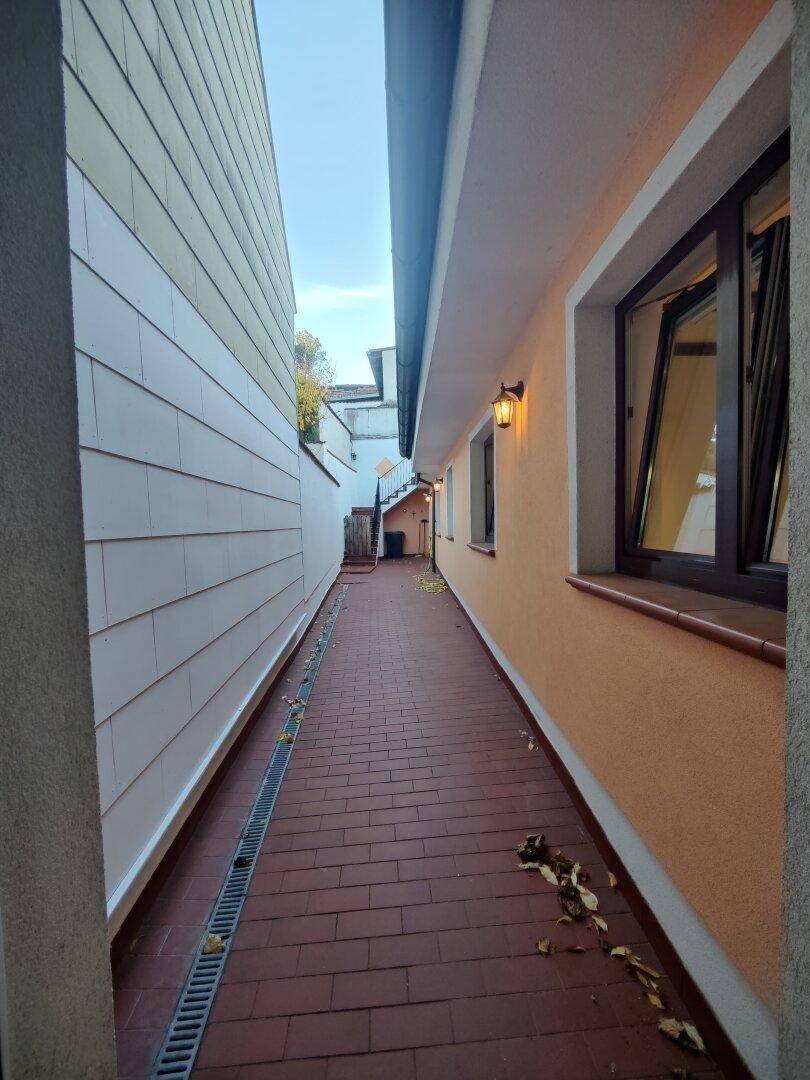 Schmaler gepflasterter Gang zwischen zwei Gebäuden mit Entwässerungsrinne.