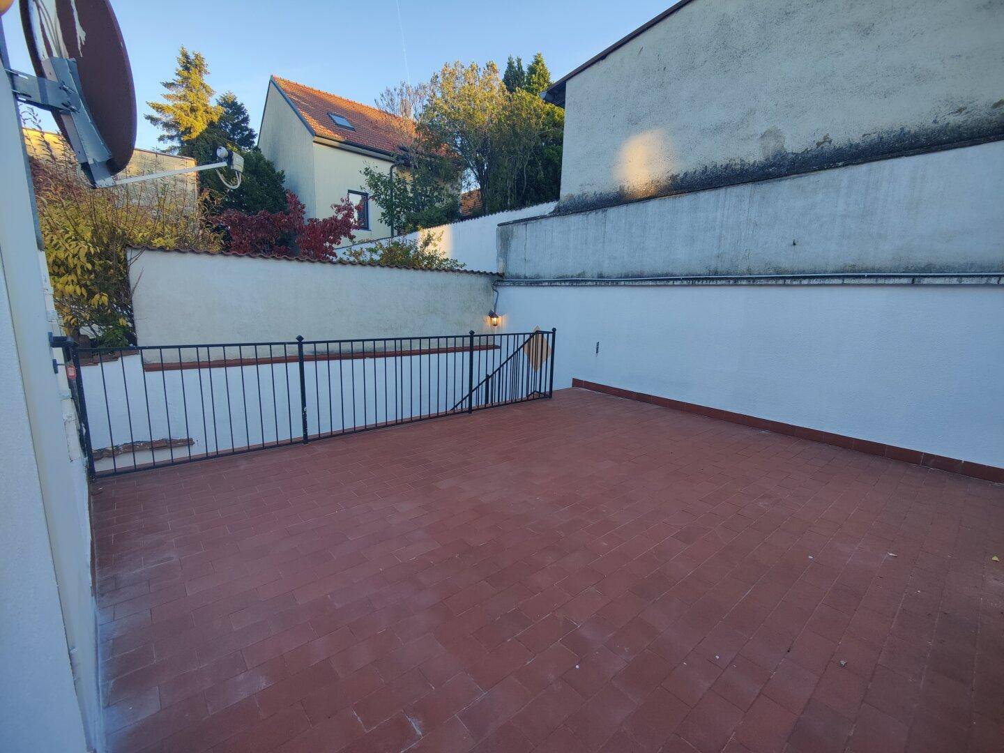 Weitläufige Außenterrasse mit roten Fliesen und schützendem Geländer, ideal für Entspannung.