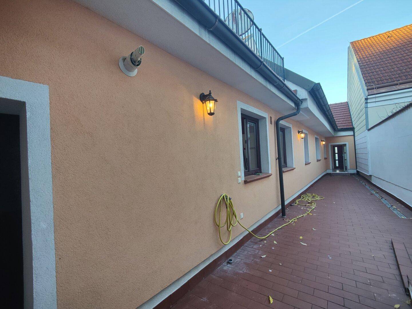 Außenansicht des Gebäudes mit orangefarbener Fassade, Fenstern und gepflastertem Zugangsweg.