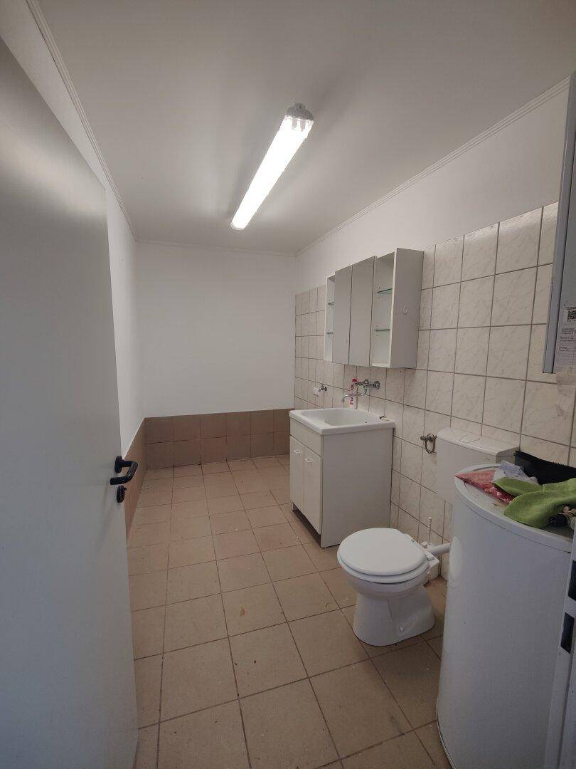 Kleines WC mit Toilette, Waschbecken und Spiegelschrank, teilweise gefliest.