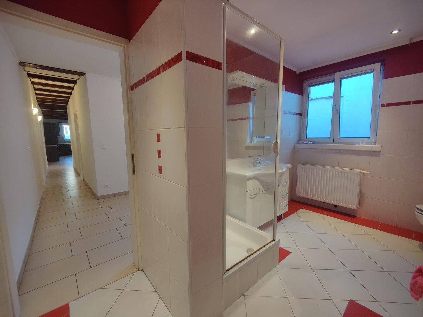 Modernes Badezimmer mit Duschkabine, Waschtisch und auffälligen rot-weißen Fliesen.